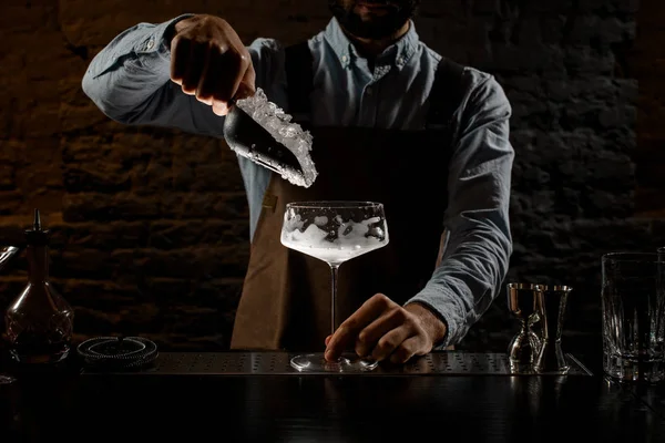 Профессиональный бармен кладет дробленый лед в большой коктейльный бокал специальной ложкой — стоковое фото