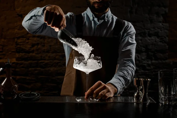 Профессиональный бармен кладет дробленый лёд в большой коктейльный бокал специальной ложкой — стоковое фото