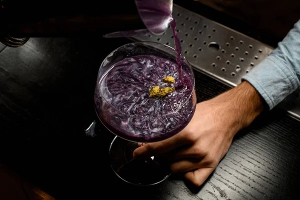 黄色の花と大きなカクテルグラスに紫色のアルコール飲料を注ぐバーテンダー — ストック写真