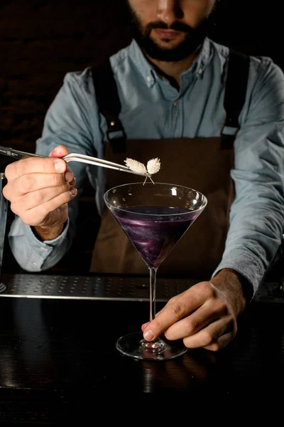 Bartender decorated purple alcoholic cocktail in a martini glass with a flower by tweezers — 스톡 사진