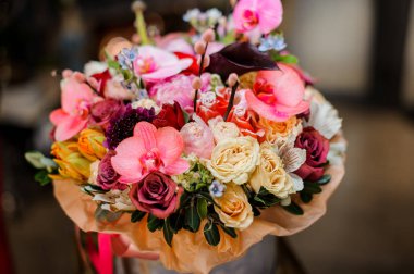 Gri kutu farklı renkte güller, sarı laleler ve altın kağıda sarılı pembe orkide dallarıyla dolu.