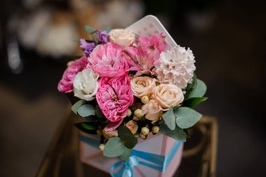 Beyaz, kremsi renklerle dolu mavi bantlı yumuşak bir kutu ve yeşil yapraklarla süslenmiş pembe güller.