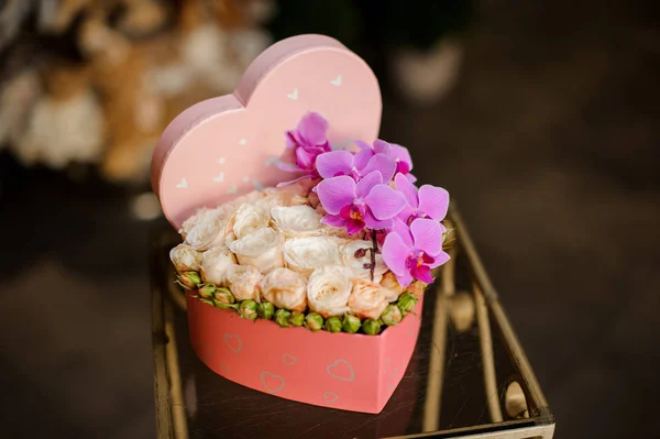 Szív alakú doboz tele krémes színű rózsák a zárt rügyek és ága a rózsaszín orchideák — Stock Fotó