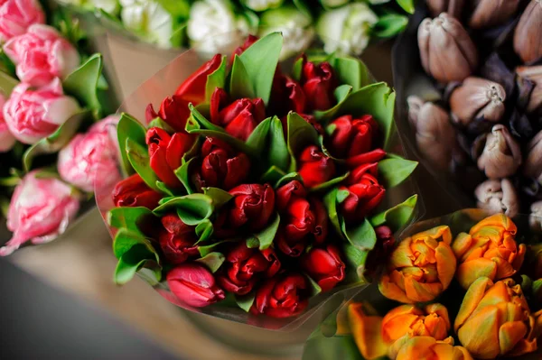 Beautiful bouquets of pink, orange and red tulips with a green leaves in the transparent wrapping paper