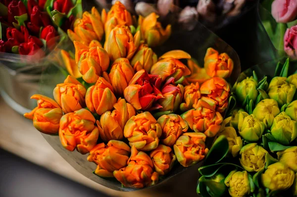 Krásné kytice ze žlutých, oranžových a červených tulipánů se zelenými listy v průhledném balicím papíru — Stock fotografie