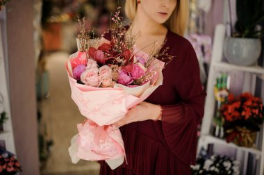 Güller ve şakayıklardan oluşan buketi olan kızın yakın çekimi.