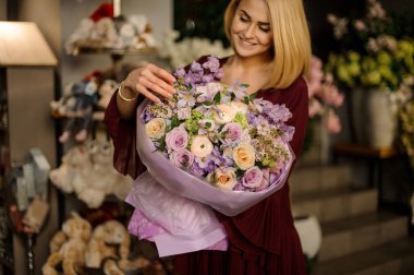 İyi giyimli bir kadın çiçek buketine bakıyor.