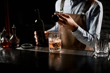 Profesyonel barmen bardaktan bardağa altın alkollü bir içecek dolduruyor.