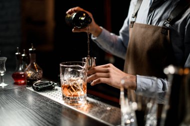 Barmen alkollü bir içeceği şişeden bir jigger 'a dolduruyor.