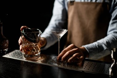 Profesyonel barmen elinde küçük bir martini bardağı ve ölçü kabıyla kokteyl tutuyor.