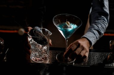 Profesyonel barmen, çivili martini bardağında mavi alkollü kokteyl servis ediyor.