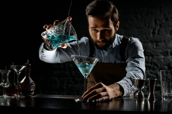 Barista maschile versando un cocktail alcolico di colore blu dal misurino con colino a un bicchiere da martini — Foto Stock