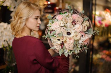 Elinde bir buket yumuşak krem rengi çiçek tutan kız ambalaj kağıdında yapraklarla süslenmiş.