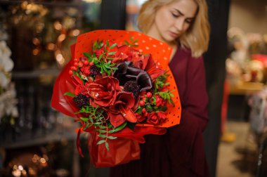 Paket kağıdında yapraklar ve böğürtlenlerle dolu bahar çiçeği tutan bir kız.