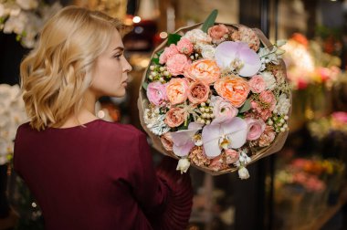 Beyaz böğürtlenlerle süslenmiş pembe gül ve orkidelerden oluşan bir buket tutan kadın.