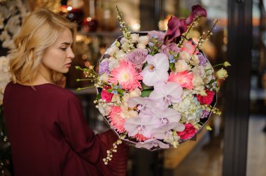 Elinde bir buket pembe meyve bahçesi, ortanca ve dallarla süslenmiş güller tutan bir kız.