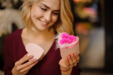 Gülen kız elinde beyaz tüyler ve pembe güllerle dolu küçük bir kalp şeklinde bir kutu tutuyor.