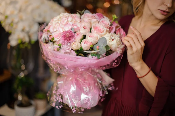 Paket kağıdında bir buket pembe gül tutan bir kız.