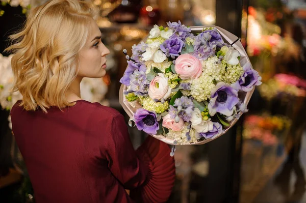 Paket kağıdında bahar demeti tutan yumuşak mor, yeşil ve pembe renkli çiçekler tutan bir kız.