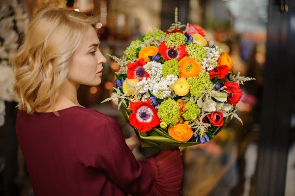 Mujer sosteniendo un ramo de flores blancas, verdes, naranjas y rojas en el papel de regalo — Foto de Stock