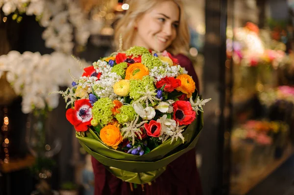 Chica sonriente sosteniendo un ramo de primavera de flores blancas, verdes, naranjas y rojas en el papel de envolver —  Fotos de Stock