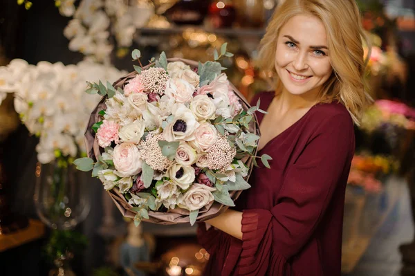 Lächelndes Mädchen mit einem Strauß zarter cremiger Blüten, die mit Blättern im Packpapier verziert sind — Stockfoto