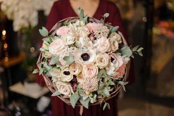 Elinde bir buket yumuşak krem rengi çiçek tutan kadın ambalaj kağıdındaki yapraklarla süslenmiş.