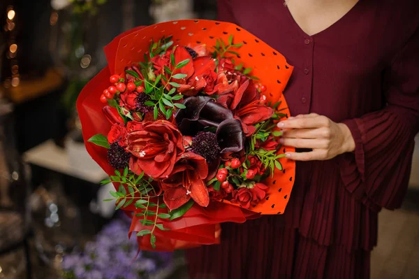 Mujer sosteniendo un ramo de amarilis de color rojo brillante con hojas y bayas en el papel de regalo —  Fotos de Stock