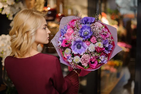 Flicka som håller i en vårbukett av mörklila, rosa och rosiga blommor i omslagspappret — Stockfoto