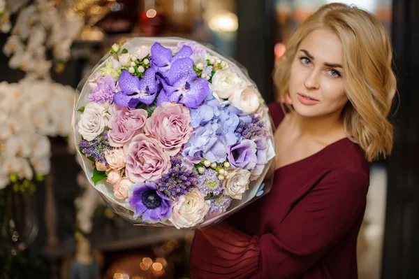 Chica sosteniendo un ramo de primavera de orachids púrpura, hortensias y rosas cremosas envolver en papel — Foto de Stock