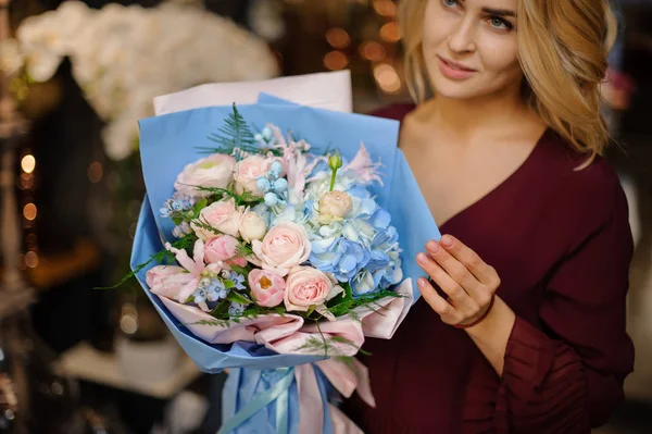 Girl holding a spring bouquet of blue hydrangeas and creamy roses wrap in paper with green leaves — 스톡 사진