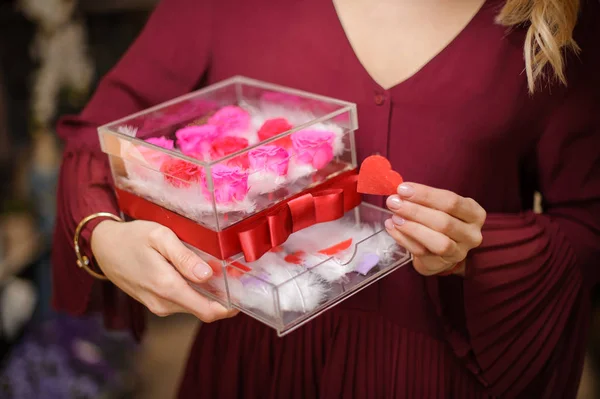 Woman holding a plastic transparent box full of white feathers and red and pink roses — 스톡 사진