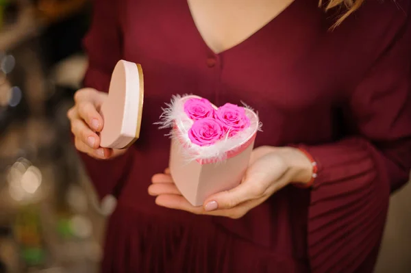 Mujer sosteniendo una pequeña caja con forma de corazón llena de plumas blancas y rosas rosas — Foto de Stock