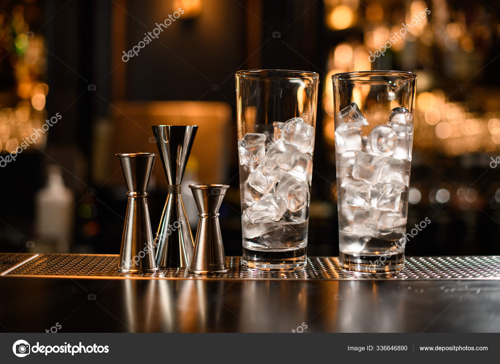 Two tall cocktail glasses half full of ice and metal jiggers on the bar  counter Stock Photo by ©Fesenko 336646890