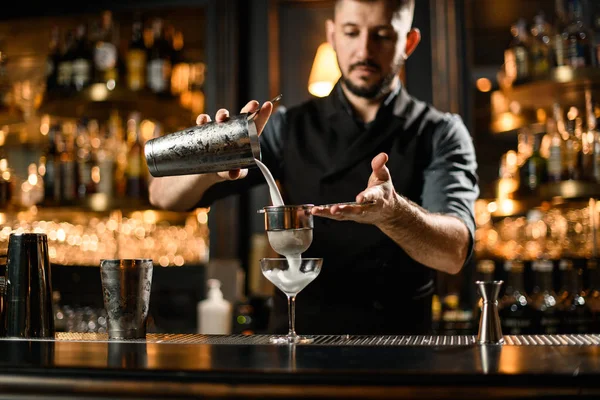 Barman masculino derramando uma bebida alcoólica coquetel da coqueteleira de aço através da peneira — Fotografia de Stock