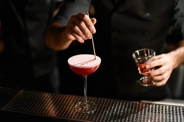 Professional bartender decorated a pink cocktail the a white scum with a liquor on the toothpick — 스톡 사진