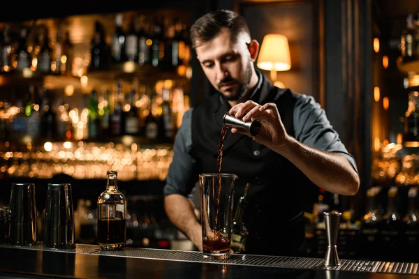 Cantinero profesional sirviendo una bebida alcohólica marrón del jigger a una copa de cóctel —  Fotos de Stock