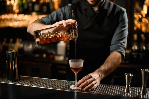 Barman profissional derramando uma bebida alcoólica marrom do copo através do filtro — Fotografia de Stock