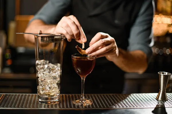 Barman profissional decorando um coquetel marrom no copo com uma folha seca por um pino — Fotografia de Stock