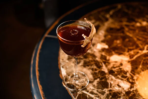 Brown cocktail in the glass decorated with a dried leaf by a pin on the marble table — 스톡 사진