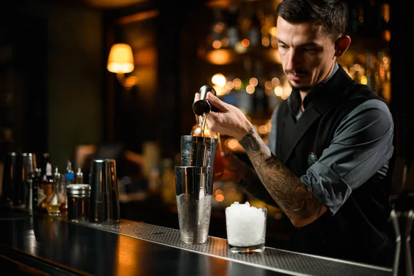 Cantinero macho sirviendo una bebida alcohólica del jigger a una coctelera de acero —  Fotos de Stock