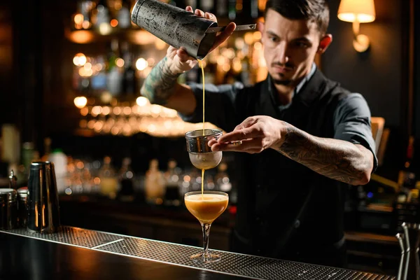 Mannelijke barman schenkt een gladde oranje alcoholische cocktaildrank uit de stalen shaker door de zeef — Stockfoto