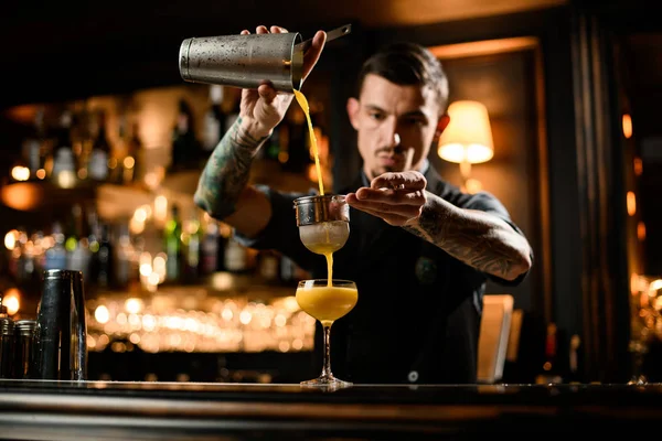 Samec barman nalévá hladký žlutý alkoholický koktejl z ocelového třepače přes síto — Stock fotografie