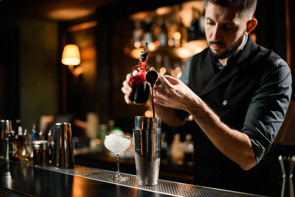 Barman schenkt een bloederige rode alcoholische drank uit het jigger in een stalen shaker met een fles — Stockfoto