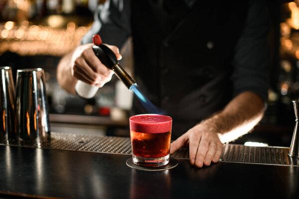 Close-up of bartender burning alcohol drink with burner