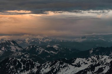Gün batımında akşam gökyüzünün altında karla kaplı dağlara bak.
