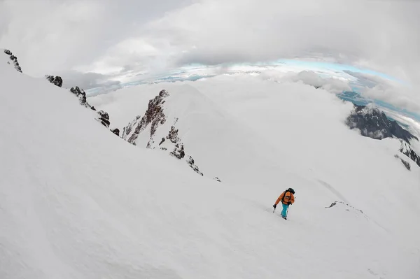 Человек с снаряжением для походов карабкается по снегу на горный холм — стоковое фото