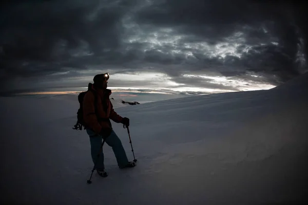 Man med vandringsutrustning står på snön på berget kulle med pinnar och ryggsäck — Stockfoto