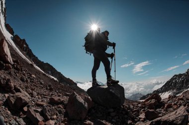 Kar etrafındaki kayaların üzerinde duran adam güneşin altında berrak gökyüzünde kalıntılar bırakıyor.