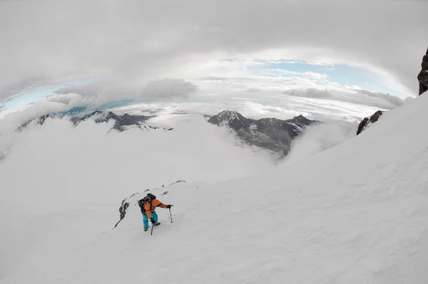 Человек с туристическим снаряжением карабкается по снегу на горный холм — стоковое фото